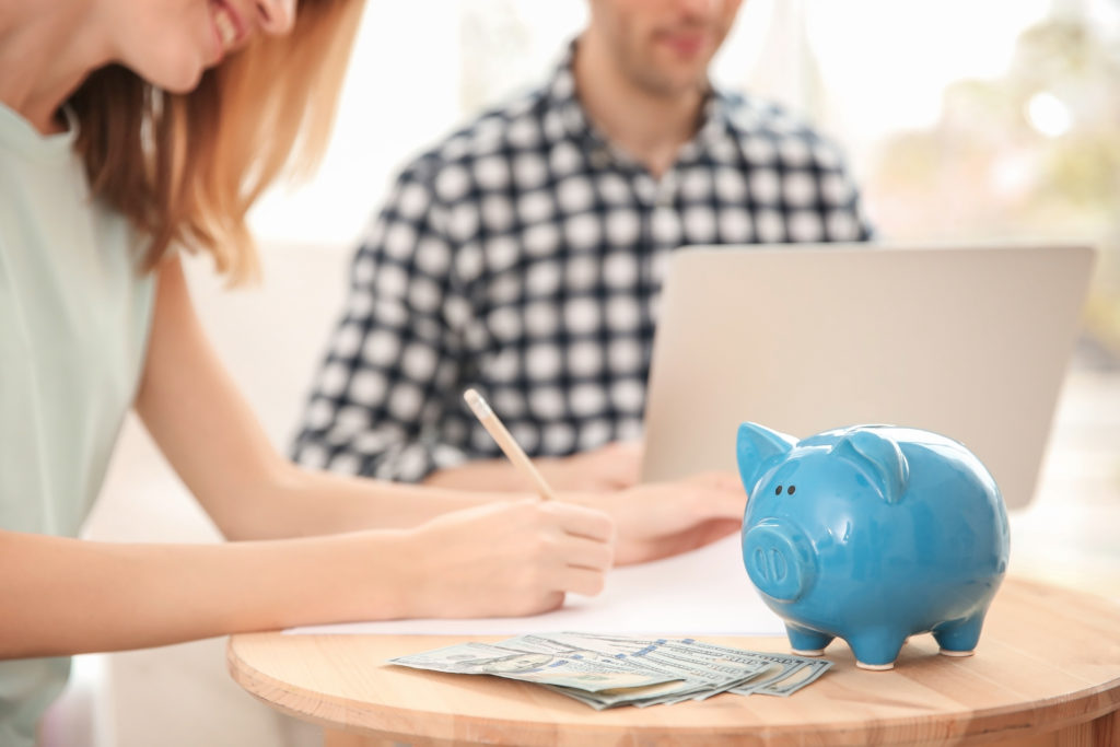 Piggy bank, money and blurred couple on background