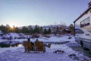 couple sitting by a pond in the snow by their RV