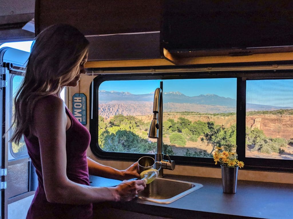 Woman doing dishes in an RV with beautiful view of Moab Utah in kitchen window