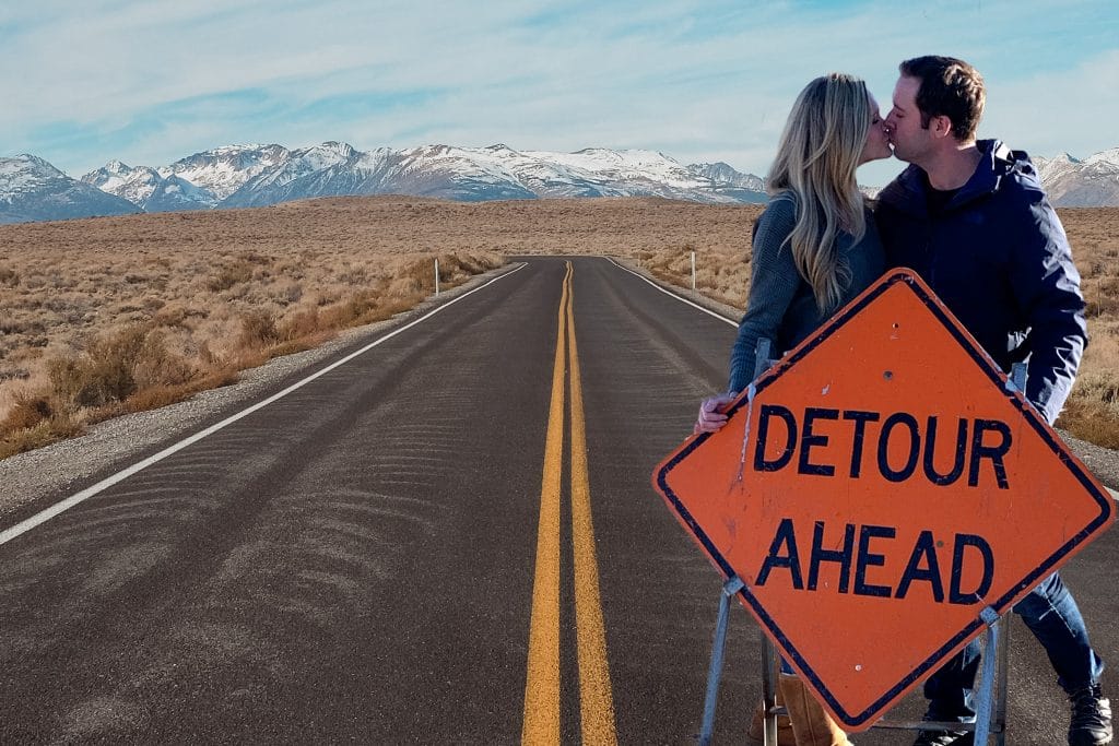 Couple standing behind a detour ahead road sign kissing