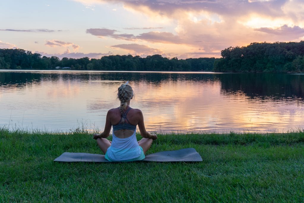 woman doing yoga by a lake at sunset