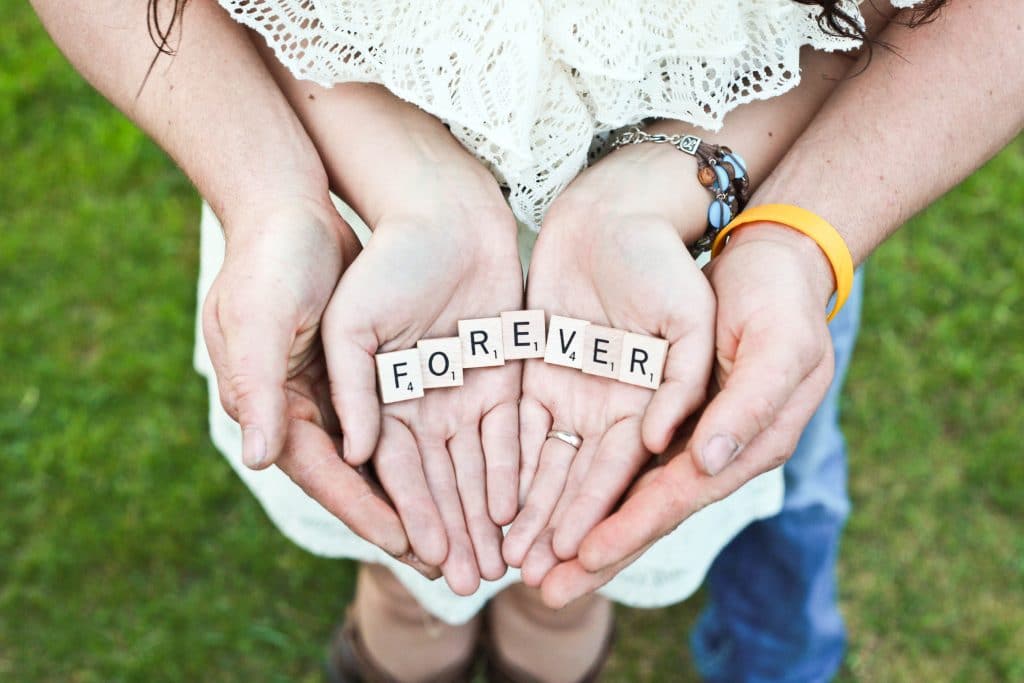 Couples hands together with scrabble tiles spelling out the word forever