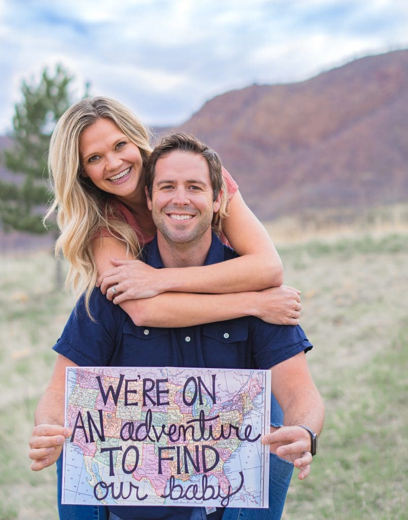 Couple holding map that says "we're on an adventure to find our baby" for domestic infant adoption announcement